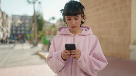 Young hispanic woman surprised using smartphone at street Stock Footage 167421973
