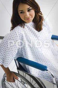 Young hispanic woman wearing hospital gown in wheelchair Stock Photos