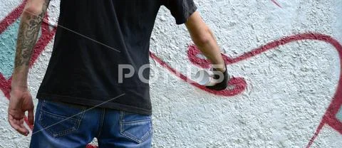 A young hooligan paints graffiti on a concrete wall. Illegal vandalism concep Stock Photos