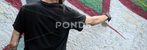 A young hooligan paints graffiti on a concrete wall. Illegal vandalism concep Stock Photos