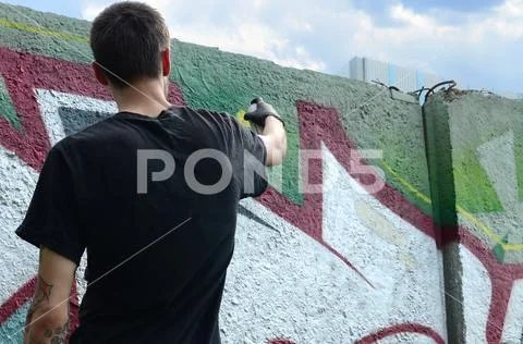 A young hooligan paints graffiti on a concrete wall. Illegal vandalism concep Stock Photos