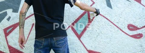 A young hooligan paints graffiti on a concrete wall. Illegal vandalism concep Stock Photos