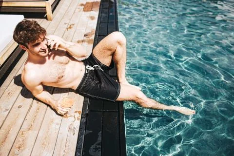 Young hot man resting at swimpool. Sexy guy lying on edge near water and talking Stock Photos
