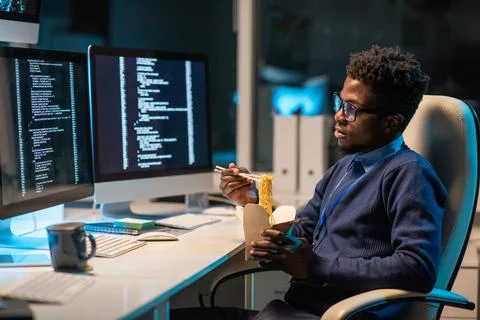 Young hungry programmer eating chinese wok in front of computer screen with Stock Photos