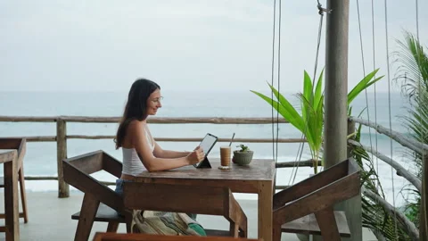 Young illustrator drawing on tablet at cafe with ocean view, palm trees. Pretty Stock Footage 252690906