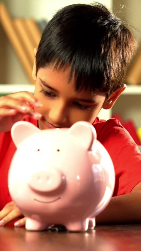 Young Indian boy placing coins in piggy bank at home Stockbeeldmateriaal 343214559
