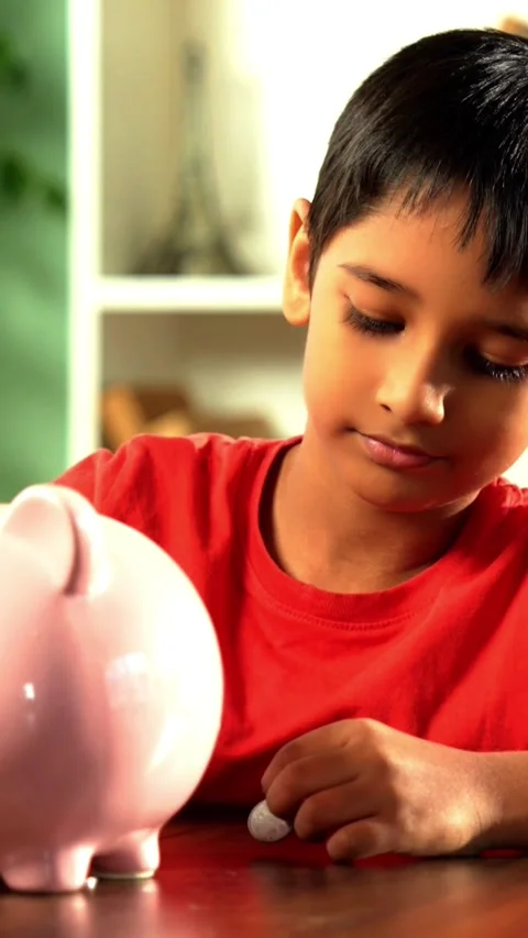Young Indian boy placing coins in piggy bank at home Stock Footage 343214568