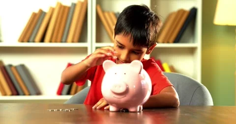Young Indian boy placing coins in piggy bank at home Stock Footage 343215228