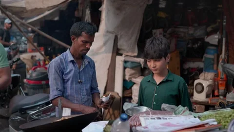 A young Indian boy purchasing roasted peanuts on a roadside hand cart Stock Footage 328501406