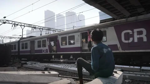 A young Indian boy sitting next to a railway track with local train passing Vídeo Stock 331922991