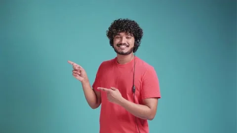 Young indian call center agent man using headset in coral t-shirt on blue studio Stock Footage 238620154