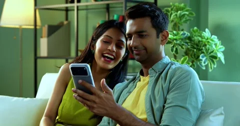 Young Indian couple browsing mobile phone together while relaxing on sofa Stock Footage 342692631