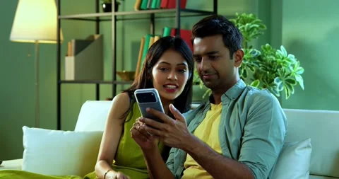 Young Indian couple browsing mobile phone together while relaxing on sofa Stock Footage 342692652