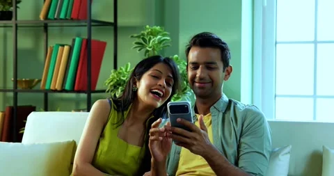 Young Indian couple browsing mobile phone together while relaxing on sofa Stock Footage 342692691
