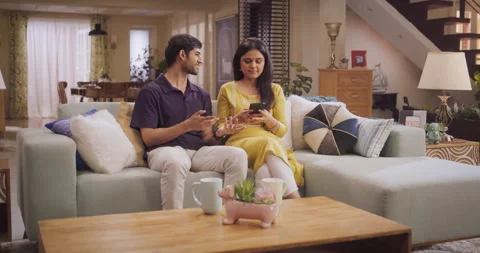 Young Indian Couple Using Smartphone sitting on Sofa at Hom Vídeo Stock 241904126