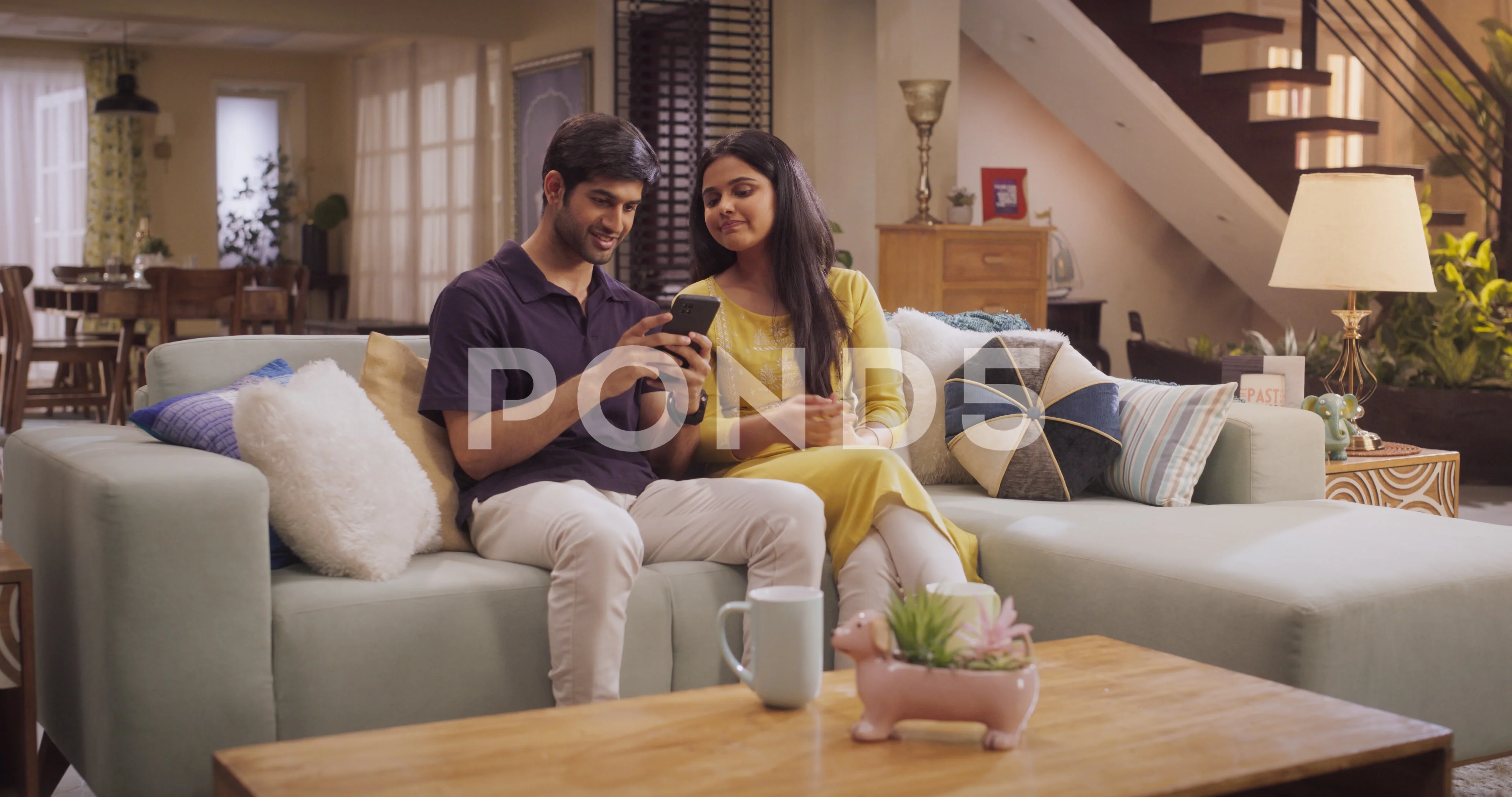 Young Indian Couple Using Smartphone sitting on Sofa at Home