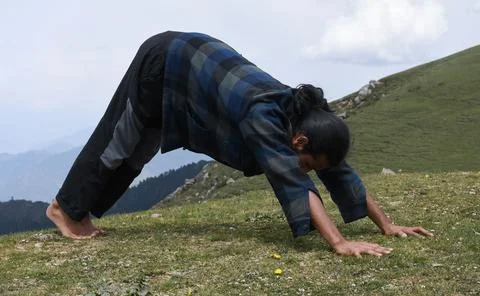 A young Indian guy doing Adho Mukha Svanasana ​yoga pose in the top of mountain. Foto stock