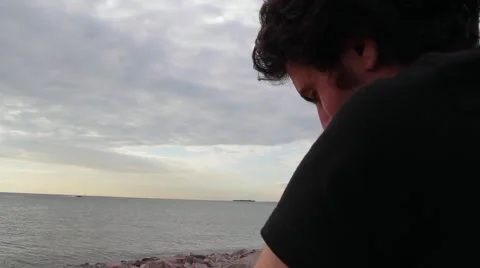 A young indian look man sitting on the stone beach looking forward on the sea Stock Footage 66474576