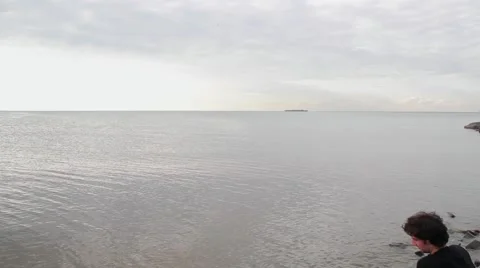 A young indian look man sitting on the stone beach looking forward on the sea Stock Footage 66475154