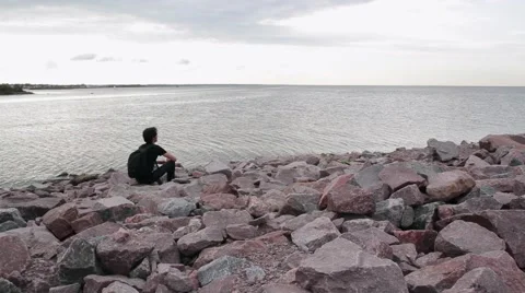 A young indian look man sitting on the stone beach looking forward on the sea Stock Footage 66475754