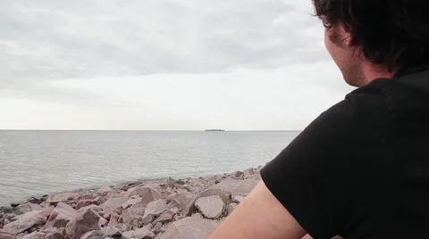 A young indian look man sitting on the stone beach looking forward on the sea Stock Footage 66475944