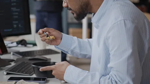 Young Indian Male Developer Eating Lunch at Workstation in front of PC Stock Footage 337476941