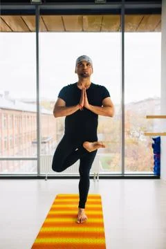 Young Indian man doing a tree pose during yoga practice Stock Photos