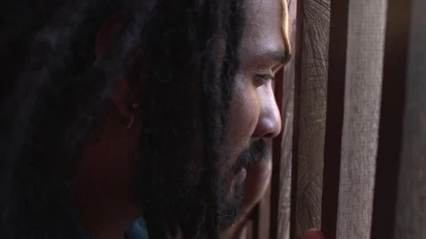 Young indian man with dreadlocks behind a fence, wistful look, prisoner Stock Footage 167761323