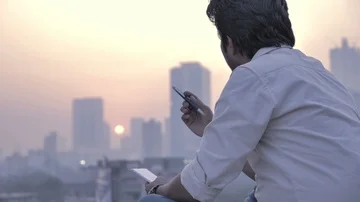 A young Indian man holding a notepad and pen against the city skyline, India Stock Footage 85877487