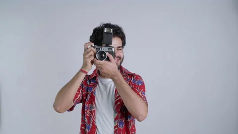 Young Indian man holding SLR camera pointing at lens against white background Stock Footage 170573853