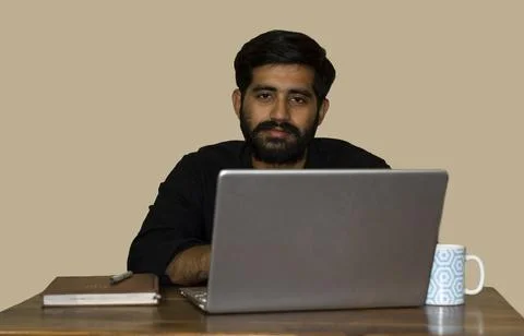 A young indian man looking at the camera while working on laptop. Stock Photos