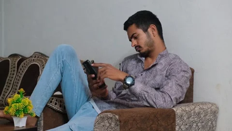 Young Indian man looking stressed and tired while using his smartphone at home Видео 330390959