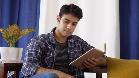 Young Indian man reading a book and attending an urgent call Stock Footage 120825909