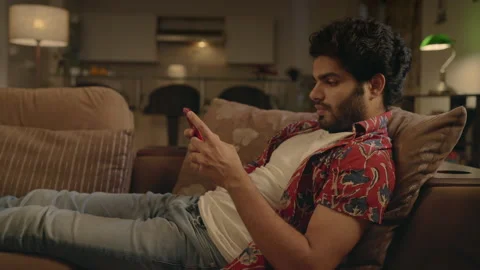 Young Indian man resting on a couch using mobile phone at house. Stock Footage 170572690