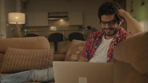 Young Indian man sitting on couch watching a Comedy Movie on a laptop at home Stock Footage 170574500