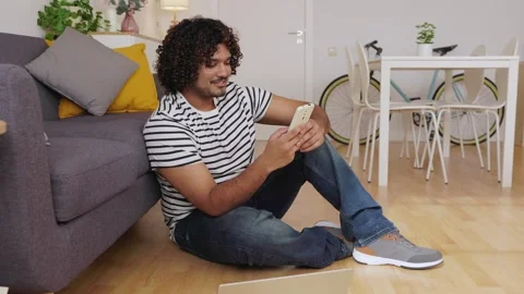 Young Indian man sitting on floor using phone Stock Footage 345096120