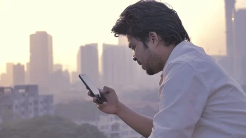 A young Indian man typing a text message on his phone against the city skyline Stock Footage 85874835