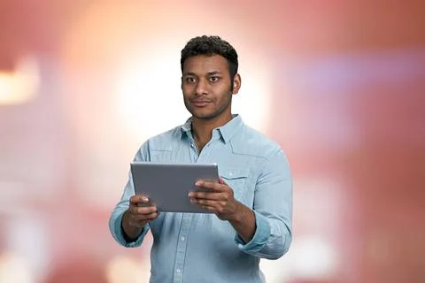 Young indian man using digital tablet on abstract pink bokeh background. Stock Photos