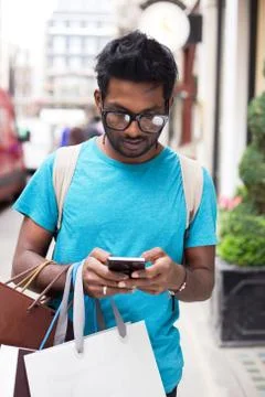 Young indian man using his phone and holding shopping bags Stock Photos