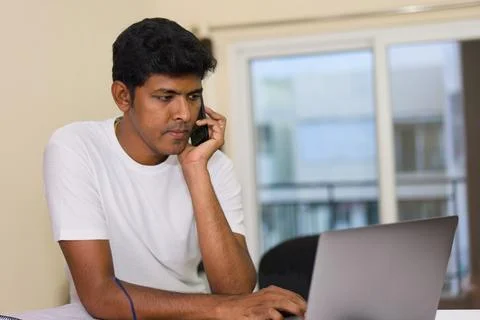 Young indian man using laptop and talking on the phone at home Stock Photos