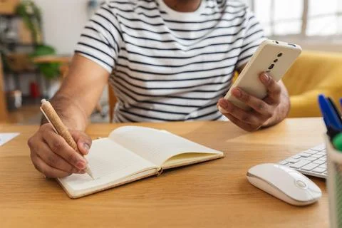 Young Indian man using mobile phone and writing notes Stock Photos