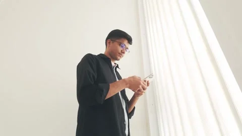 Young Indian man using smartphone indoors, smiling while browsing or texting. Stock Footage 305450349