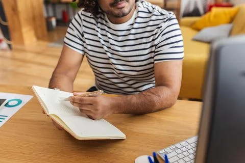 Young Indian man writing in notebook at study desk Stock Photos