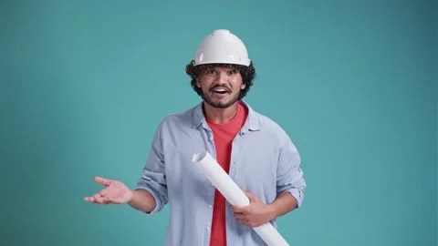 Young indian or arabic engineer standing holding helmet, blueprint and wearing Stock Footage 238772130