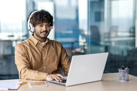 Young indian programmer working inside office with laptop, man in headphones Stock Photos