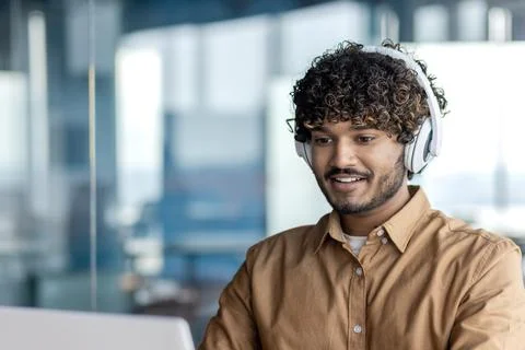Young indian programmer working inside office with laptop, man in headphones Stock Photos