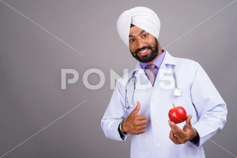 Young Indian Sikh man doctor smiling and holding apple Stock Photos