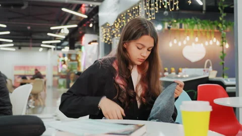 Young individual concentrating on notes amidst cozy coffee shop setting. Student Stock Footage 331361856