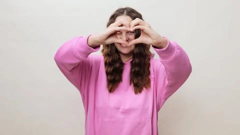 A young individual joyfully creates a heart shape with their hands, wearing a Stock Footage 302829309