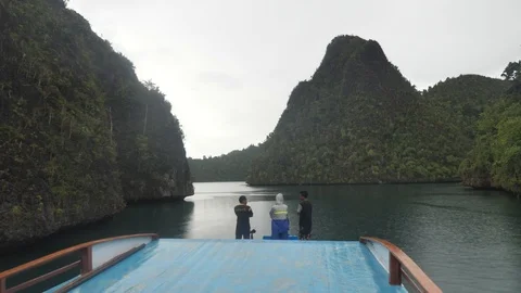 Young Indonesian Men Standing At Front Of Boat Traveling Through Wayag Islands Stock Footage 98826480
